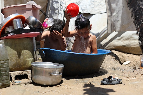 أطفال فلسطينيون نازحون يحاولون التخفيف من حرارة الصيف داخل خيمة مهترئة في مخيم النصيرات وسط قطاع غزة. تصوير: حسن الجديدي
