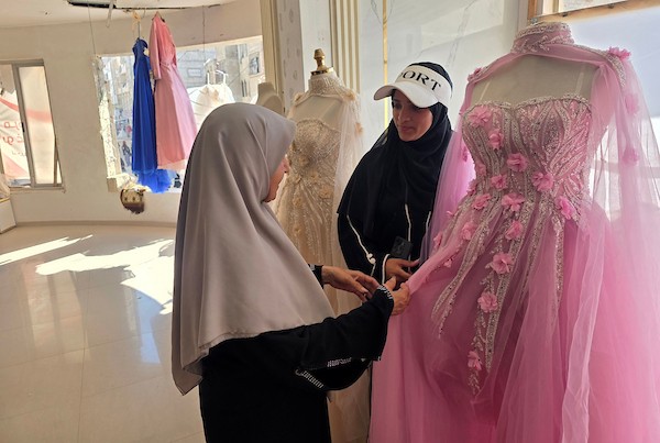 زبائن يتصفحون فساتين وبدلات زفاف داخل متجر في خان يونس، جنوبي قطاع غزة، في 1 يونيو/حزيران 2026، حيث يواصل الفلسطينيون التمسك بطقوس الزواج رغم الحرب والدمار والظروف المعيشية القاسية. تصوير: طارق محمد