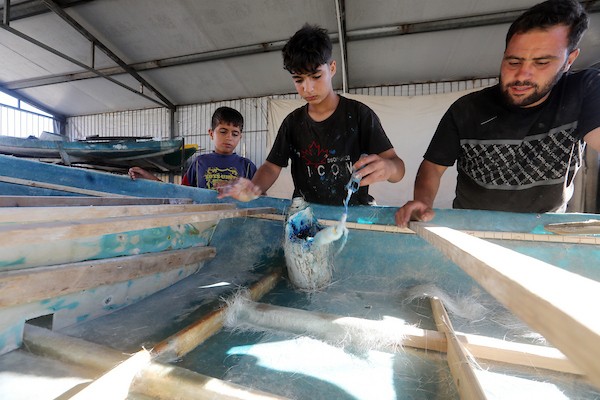 الفلسطيني عطية مقداد وأفراد من عائلته يصلحون قوارب تضررت جراء الغارات الإسرائيلية في ميناء غزة، في 2 يونيو/حزيران 2026. ويستخدمون أخشاباً جرى إنقاذها من المباني المدمّرة لصيانة القوارب وصنع المجاديف.تصوير: بلال أسامة