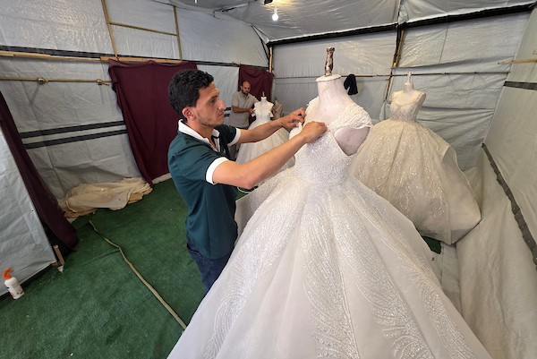 زبائن يتصفحون فساتين وبدلات زفاف داخل متجر في خان يونس، جنوبي قطاع غزة، في 1 يونيو/حزيران 2026، حيث يواصل الفلسطينيون التمسك بطقوس الزواج رغم الحرب والدمار والظروف المعيشية القاسية. تصوير: طارق محمد