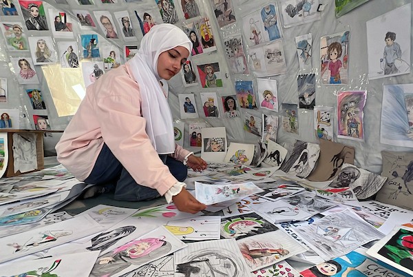 الفنانة الفلسطينية رنيم ناصر تعرض رسوماتها داخل خيمتها في دير البلح وسط قطاع غزة، موثّقةً بالألوان معاناة الحرب والنزوح. تصوير: يوسف أبو وطفة