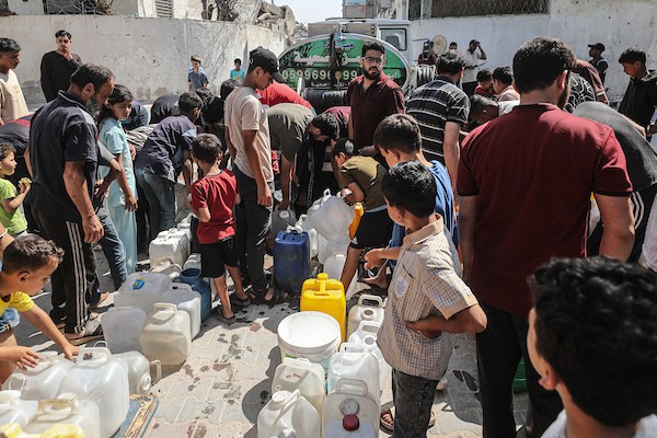 فلسطينيون نازحون ينتظرون دورهم للحصول على مياه من شاحنة توزيع متنقلة في مخيم البريج وسط قطاع غزة، تصوير: معز صالحي