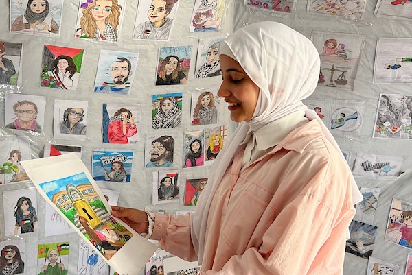الفنانة الفلسطينية رنيم ناصر تعرض رسوماتها داخل خيمتها في دير البلح وسط قطاع غزة، موثّقةً بالألوان معاناة الحرب والنزوح. تصوير: يوسف أبو وطفة