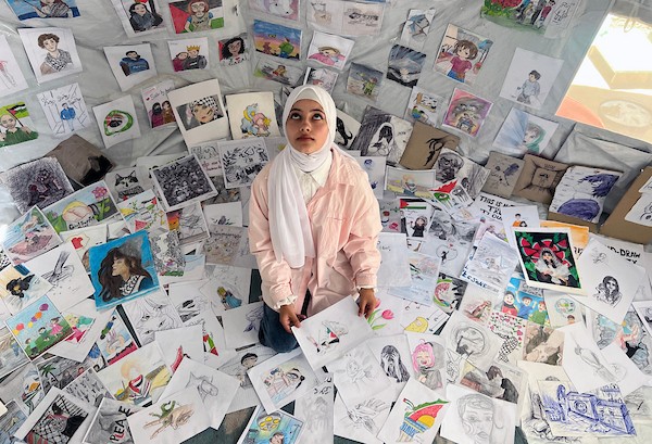 الفنانة الفلسطينية رنيم ناصر تعرض رسوماتها داخل خيمتها في دير البلح وسط قطاع غزة، موثّقةً بالألوان معاناة الحرب والنزوح. تصوير: يوسف أبو وطفة