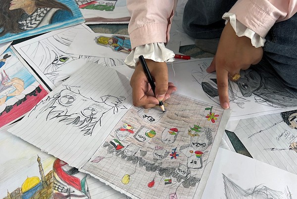 الفنانة الفلسطينية رنيم ناصر تعرض رسوماتها داخل خيمتها في دير البلح وسط قطاع غزة، موثّقةً بالألوان معاناة الحرب والنزوح. تصوير: يوسف أبو وطفة