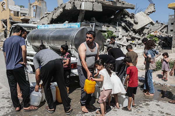 فلسطينيون نازحون ينتظرون دورهم للحصول على مياه من شاحنة توزيع متنقلة في مخيم البريج وسط قطاع غزة، تصوير: معز صالحي