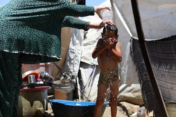 أطفال فلسطينيون نازحون يحاولون التخفيف من حرارة الصيف داخل خيمة مهترئة في مخيم النصيرات وسط قطاع غزة. تصوير: حسن الجديدي