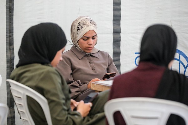 في مخيم البريج وسط قطاع غزة، يجلس طلبة فلسطينيون أمام هواتفهم وأجهزتهم لأداء امتحانات “التوجيهي” إلكترونيًا. صورة: معز صالحي