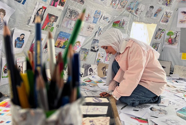 الفنانة الفلسطينية رنيم ناصر تعرض رسوماتها داخل خيمتها في دير البلح وسط قطاع غزة، موثّقةً بالألوان معاناة الحرب والنزوح. تصوير: يوسف أبو وطفة
