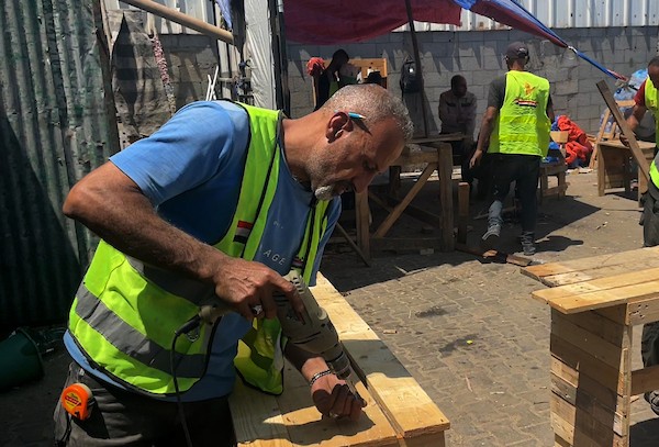 في ورشة عمل بدير البلح، وسط قطاع غزة، بتاريخ 31 مايو/أيار 2026، قام عمال فلسطينيون بتصنيع مقاعد مدرسية من منصات خشبية معاد تدويرها كانت تُستخدم في المساعدات. (صورة: يوسف أبو وطفة)