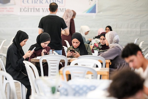في مخيم البريج وسط قطاع غزة، يجلس طلبة فلسطينيون أمام هواتفهم وأجهزتهم لأداء امتحانات “التوجيهي” إلكترونيًا. صورة: معز صالحي