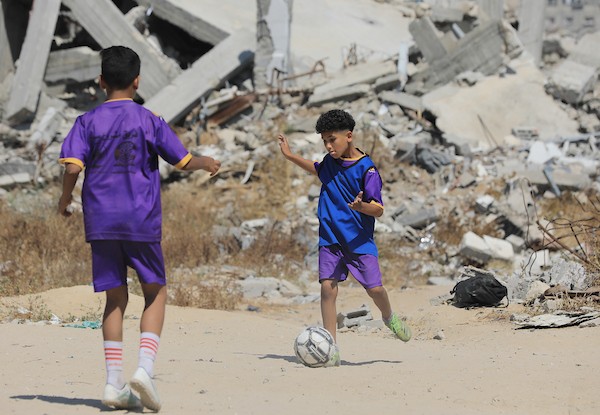 أطفال فلسطينيون نازحون يرتدون الزي الرياضي يشاركون في حصة تدريبية لكرة القدم مع مدربهم في ساحة صغيرة وسط أنقاض المنازل المدمرة في حي الشيخ رضوان بمدينة غزة، 16 حزيران/يونيو 2026. تصوير: بلال أسامة