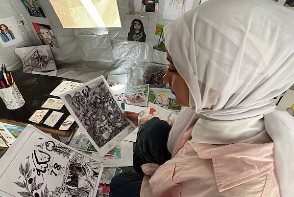 الفنانة الفلسطينية رنيم ناصر تعرض رسوماتها داخل خيمتها في دير البلح وسط قطاع غزة، موثّقةً بالألوان معاناة الحرب والنزوح. تصوير: يوسف أبو وطفة