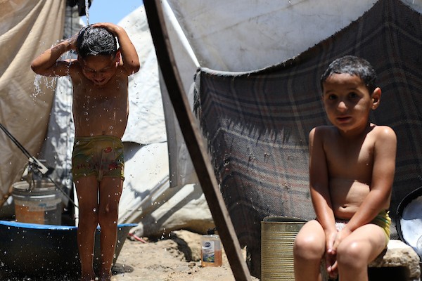 أطفال فلسطينيون نازحون يحاولون التخفيف من حرارة الصيف داخل خيمة مهترئة في مخيم النصيرات وسط قطاع غزة. تصوير: حسن الجديدي