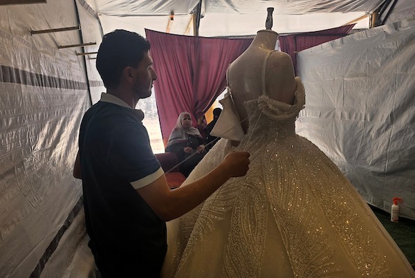 زبائن يتصفحون فساتين وبدلات زفاف داخل متجر في خان يونس، جنوبي قطاع غزة، في 1 يونيو/حزيران 2026، حيث يواصل الفلسطينيون التمسك بطقوس الزواج رغم الحرب والدمار والظروف المعيشية القاسية. تصوير: طارق محمد