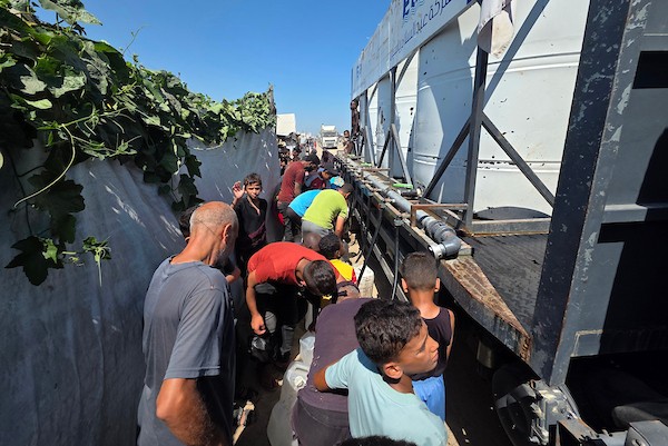 فلسطينيون يملئون خزانات المياه من شاحنة توزيع في مخيم للنازحين بمنطقة المواصي، غرب خان يونس، جنوب قطاع غزة، في 20 يوليو/تموز 2026.صورة: مأمون وزواز