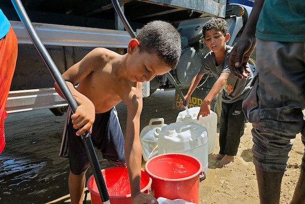 فلسطينيون يملئون خزانات المياه من شاحنة توزيع في مخيم للنازحين بمنطقة المواصي، غرب خان يونس، جنوب قطاع غزة، في 20 يوليو/تموز 2026.صورة: مأمون وزواز