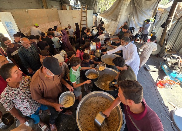 فلسطينيون نازحون يتلقون وجبات طعام مطبوخة من مطبخ خيري محلي في منطقة المواصي غربي خان يونس، جنوبي قطاع غزة، في 10 يوليو/تموز 2026. تصوير: طارق محمد