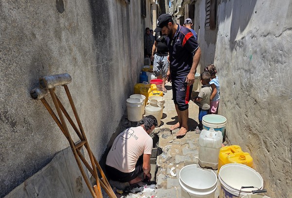 فلسطينيون ينقلون المياه في عبوات بلاستيكية من حفرة مؤقتة إلى منازلهم المتضررة في خان يونس، جنوبي قطاع غزة، وسط نقص حاد في المياه النظيفة، 11 يوليو/تموز 2026. (تصوير: طارق محمد)