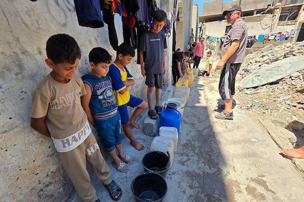 فلسطينيون ينقلون المياه في عبوات بلاستيكية من حفرة مؤقتة إلى منازلهم المتضررة في خان يونس، جنوبي قطاع غزة، وسط نقص حاد في المياه النظيفة، 11 يوليو/تموز 2026. (تصوير: طارق محمد)