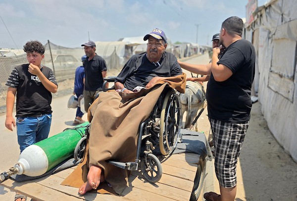 فتحي حجي، 77 عاماً، مريض كلى ويستخدم أسطوانة أكسجين، يجلس على كرسي متحرك أثناء نقله على عربة تجرها الحيوانات من منطقة بئر 19 في المواصي بمدينة خان يونس، جنوب قطاع غزة، في 22 يوليو/تموز 2026.  تصوير: طارق محمد