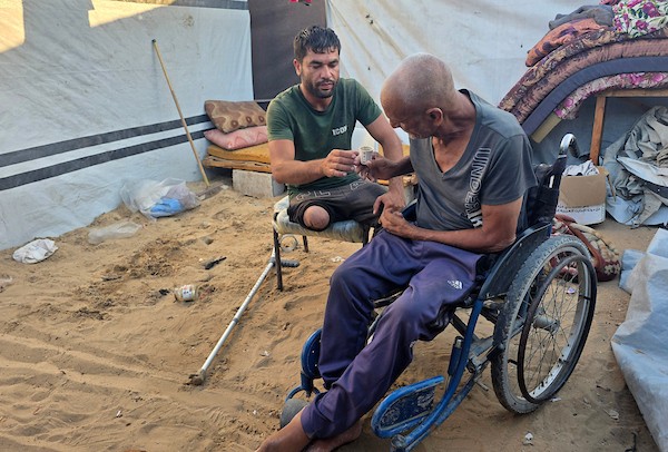 الفلسطيني فادي خليل شقورة، 32 عاماً، الذي بُترت ساقه إثر إصابته في غارة إسرائيلية سابقة، يجلس مع والديه وطفليه داخل خيمة تؤويهم في منطقة المواصي بخان يونس، جنوب قطاع غزة، في 22 يوليو/تموز 2026. تصوير: طارق محمد