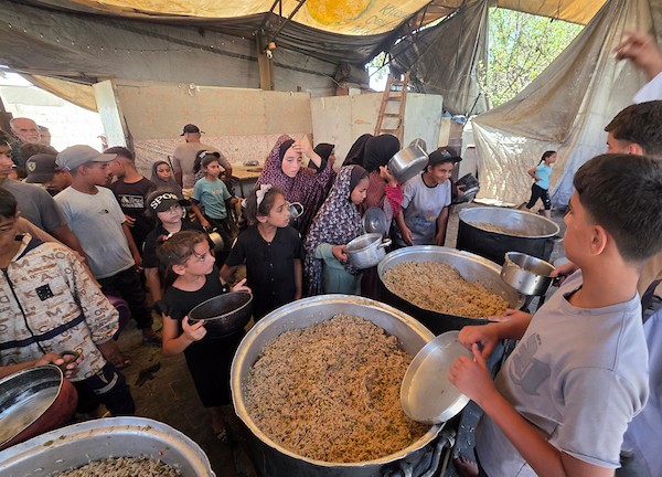 فلسطينيون نازحون يتلقون وجبات طعام مطبوخة من مطبخ خيري محلي في منطقة المواصي غربي خان يونس، جنوبي قطاع غزة، في 10 يوليو/تموز 2026. تصوير: طارق محمد