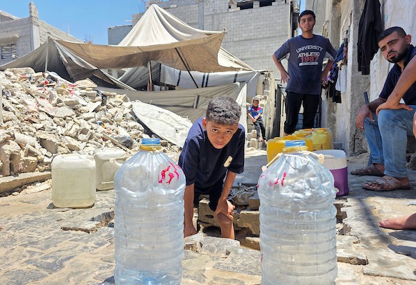 فلسطينيون ينقلون المياه في عبوات بلاستيكية من حفرة مؤقتة إلى منازلهم المتضررة في خان يونس، جنوبي قطاع غزة، وسط نقص حاد في المياه النظيفة، 11 يوليو/تموز 2026. (تصوير: طارق محمد)