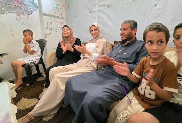 الطالبة نور عودة تحتفل مع عائلتها داخل منزل متضرر في خان يونس، بعد حصولها على معدل 99.7% في المسار العلمي وحلولها أولى على قطاع غزة وثانية على مستوى فلسطين في امتحانات التوجيهي، 24 تموز/ يوليو 2026. تصوير: طارق محمد