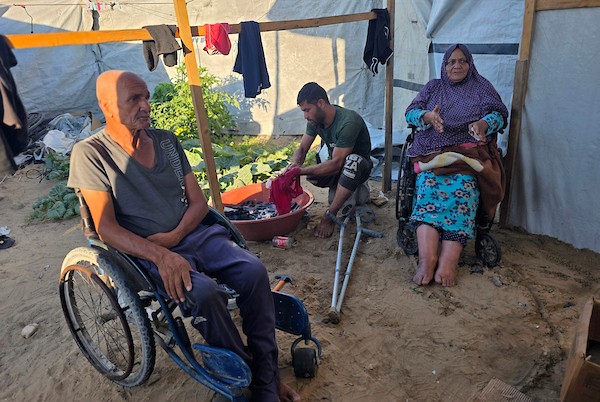 الفلسطيني فادي خليل شقورة، 32 عاماً، الذي بُترت ساقه إثر إصابته في غارة إسرائيلية سابقة، يجلس مع والديه وطفليه داخل خيمة تؤويهم في منطقة المواصي بخان يونس، جنوب قطاع غزة، في 22 يوليو/تموز 2026. تصوير: طارق محمد