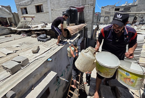 فلسطينيون ينقلون المياه في عبوات بلاستيكية من حفرة مؤقتة إلى منازلهم المتضررة في خان يونس، جنوبي قطاع غزة، وسط نقص حاد في المياه النظيفة، 11 يوليو/تموز 2026. (تصوير: طارق محمد)