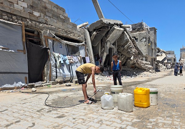 فلسطينيون ينقلون المياه في عبوات بلاستيكية من حفرة مؤقتة إلى منازلهم المتضررة في خان يونس، جنوبي قطاع غزة، وسط نقص حاد في المياه النظيفة، 11 يوليو/تموز 2026. (تصوير: طارق محمد)