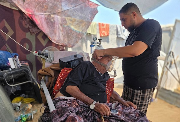 فتحي حجي، 77 عاماً، مريض كلى ويستخدم أسطوانة أكسجين، يجلس على كرسي متحرك أثناء نقله على عربة تجرها الحيوانات من منطقة بئر 19 في المواصي بمدينة خان يونس، جنوب قطاع غزة، في 22 يوليو/تموز 2026.  تصوير: طارق محمد