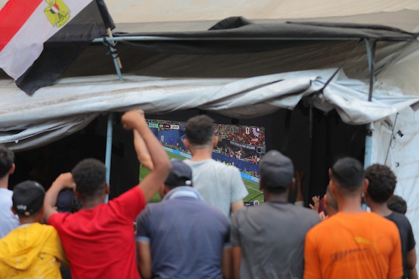 يشاهد فلسطينيون مباراة كرة قدم بين منتخبي مصر والأرجنتين داخل خيمة في مأوى تابع لوكالة (الأونروا) في مخيم النصيرات للاجئين، وسط قطاع غزة، في 7 يوليو/تموز 2026.(صورة حسن الجدي)