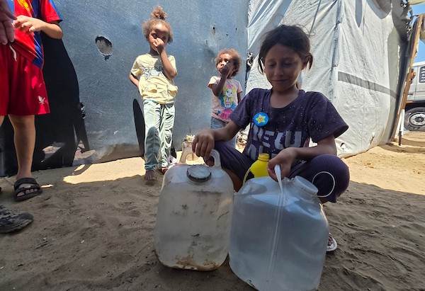فلسطينيون يملئون خزانات المياه من شاحنة توزيع في مخيم للنازحين بمنطقة المواصي، غرب خان يونس، جنوب قطاع غزة، في 20 يوليو/تموز 2026.صورة: مأمون وزواز