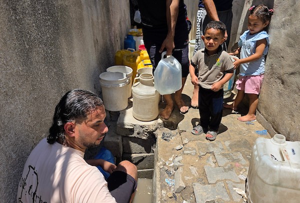 فلسطينيون ينقلون المياه في عبوات بلاستيكية من حفرة مؤقتة إلى منازلهم المتضررة في خان يونس، جنوبي قطاع غزة، وسط نقص حاد في المياه النظيفة، 11 يوليو/تموز 2026. (تصوير: طارق محمد)
