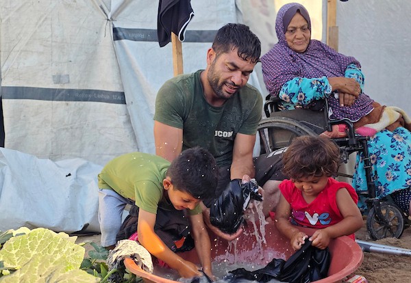 الفلسطيني فادي خليل شقورة، 32 عاماً، الذي بُترت ساقه إثر إصابته في غارة إسرائيلية سابقة، يجلس مع والديه وطفليه داخل خيمة تؤويهم في منطقة المواصي بخان يونس، جنوب قطاع غزة، في 22 يوليو/تموز 2026. تصوير: طارق محمد