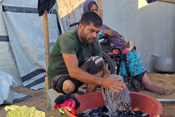 الفلسطيني فادي خليل شقورة، 32 عاماً، الذي بُترت ساقه إثر إصابته في غارة إسرائيلية سابقة، يجلس مع والديه وطفليه داخل خيمة تؤويهم في منطقة المواصي بخان يونس، جنوب قطاع غزة، في 22 يوليو/تموز 2026. تصوير: طارق محمد