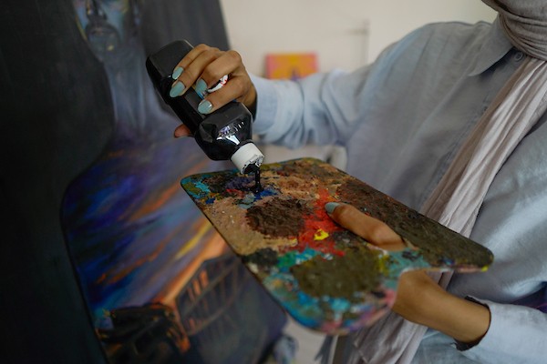 الفنانة نورة القصاص ترسم داخل غرفة بسيطة حولتها إلى مرسم في منزل أحد أقاربها بحي الشيخ رضوان في مدينة غزة، في 12 أغسطس/آب 2026. (تصوير: محمد أبو القمصان)