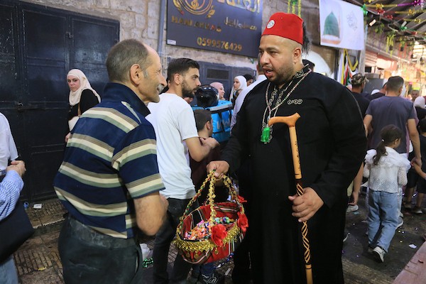 فلسطينيون بالزي التقليدي يؤدون أناشيد ومدائح دينية ويوزعون الحلوى في السوق المركزي بالبلدة القديمة في نابلس،خلال إحياء ذكرى المولد النبوي الشريف، في 25 أغسطس/آب 2026. (تصوير: محمد ناصر)