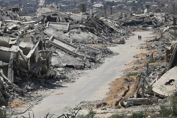 فلسطينيون يتنقلون بين أنقاض مبانٍ مدمرة في منطقة المغاري وسط قطاع غزة، في مشهد يعكس حجم الأضرار التي لحقت بالمناطق السكنية خلال الحرب. (تصوير: حسن الجدي)