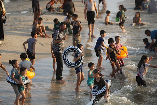 عائلات فلسطينية تقضي وقتاً على شاطئ مدينة غزة هرباً من حرارة الصيف، بينما تصطف خيام النازحين بمحاذاة الساحل، في مشهد يجمع بين البحث عن لحظة راحة وثقل النزوح والحرب، 8 أغسطس/آب 2026. (تصوير: بلال أسامة)