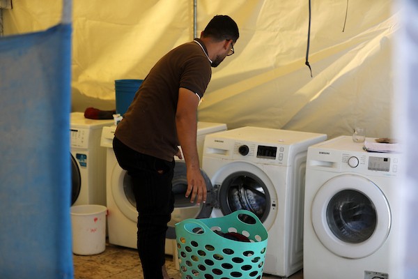 فلسطينيون يغسلون ملابسهم باستخدام غسالات كهربائية داخل مخيم للنازحين غرب مدينة غزة، في 27 أغسطس/آب 2026، وسط صعوبات في تأمين المياه والكهرباء. (تصوير: بلال أسامة)