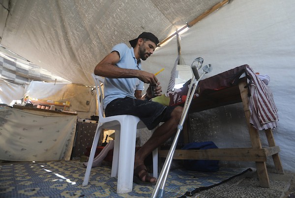 الحلاق الفلسطيني شادي البراوي، 35 عاما، يعمل داخل خيمة نزح إليها مع عائلته في مدينة غزة، في 27 آب/أغسطس 2026، بعدما فقد ساقه اليمنى إثر إصابته بشظايا خلال هجوم إسرائيلي.(تصوير: بلال أسامة)