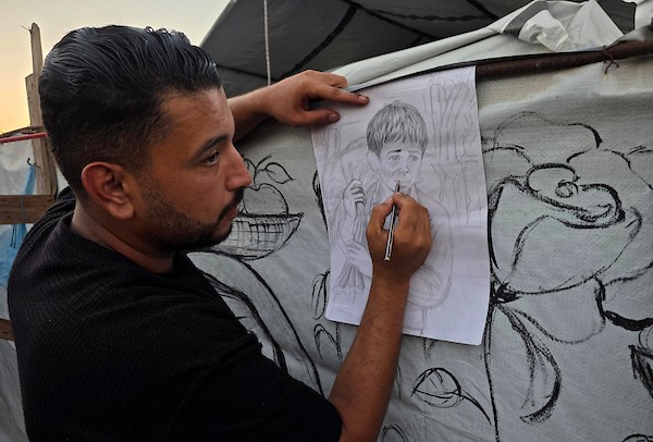 فنانون تشكيليون فلسطينيون يرسمون مشاهد تجسد الغارات والجوع ومعاناة السكان على جدران خيمة للنازحين في منطقة المواصي بخان يونس، جنوب قطاع غزة، في 9 أغسطس/آب 2026، محولين الخيمة إلى سجل بصري يوثق الحياة اليومية في ظل الحرب والنزوح. (تصوير: طارق محمد)