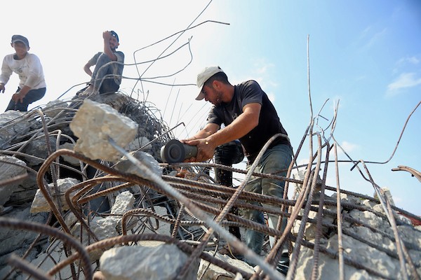 عمال فلسطينيون يستخرجون الحديد من أنقاض منازل مدمرة في حي التفاح بمدينة غزة لإعادة استخدامه في تدعيم خيام ومساكن مؤقتة للنازحين. (تصوير: بلال أسامة)