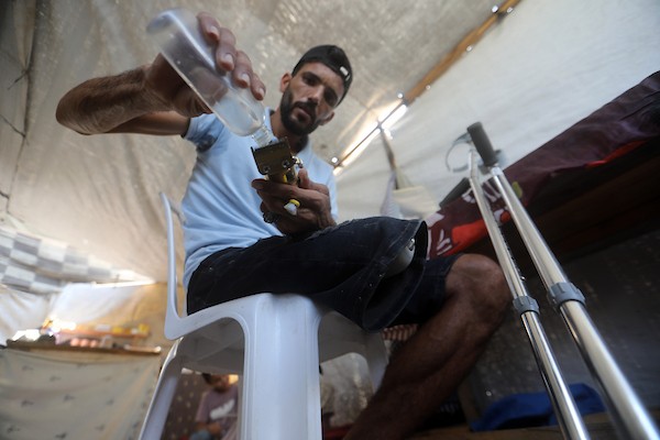 الحلاق الفلسطيني شادي البراوي، 35 عاما، يعمل داخل خيمة نزح إليها مع عائلته في مدينة غزة، في 27 آب/أغسطس 2026، بعدما فقد ساقه اليمنى إثر إصابته بشظايا خلال هجوم إسرائيلي.(تصوير: بلال أسامة)