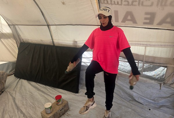 مدربة اللياقة البدنية إيمان المغير تستخدم علب طعام فارغة ومواد مهملة كأدوات رياضية خلال تدريبها داخل خيمتها في خان يونس.تصوير: طارق محمد