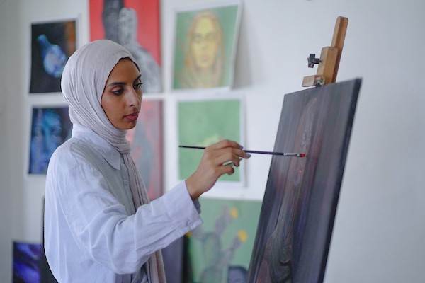 الفنانة نورة القصاص ترسم داخل غرفة بسيطة حولتها إلى مرسم في منزل أحد أقاربها بحي الشيخ رضوان في مدينة غزة، في 12 أغسطس/آب 2026. (تصوير: محمد أبو القمصان)