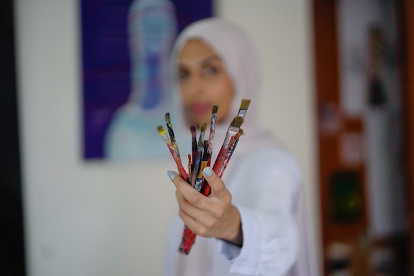 الفنانة نورة القصاص ترسم داخل غرفة بسيطة حولتها إلى مرسم في منزل أحد أقاربها بحي الشيخ رضوان في مدينة غزة، في 12 أغسطس/آب 2026. (تصوير: محمد أبو القمصان)